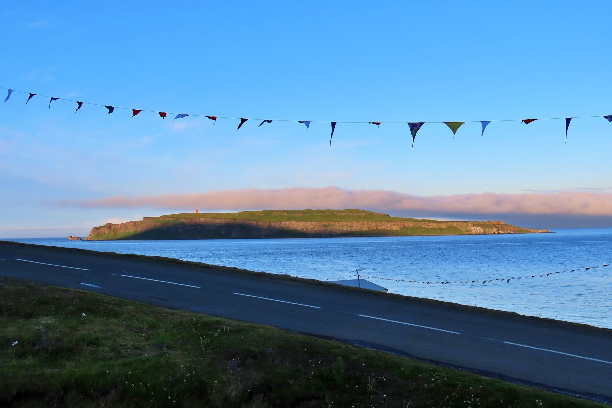 Vegur með litríkar fánar og Drangey í sólsetri